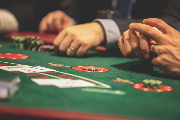 Hands playing blackjack in a casino setting with cards and chips on a green table.