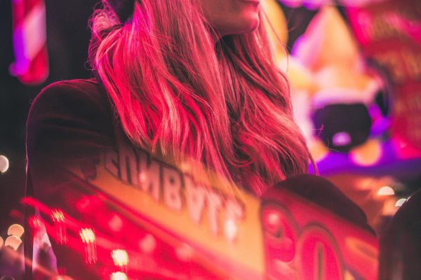 Stylish woman in urban setting with neon pink lights and casino reflections at night.